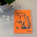 Blue line art illustration of a dog on orange paper, with its paw up in front of a ball and wearing a red collar.