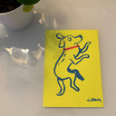 Blue line art illustration on bright yellow paper of a dog laying on its side while wearing a red collar.