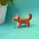 Small sculpture of a brown squirrel, with cute cartoon eyes and a buckteeth showing out its closed mouth. It stands on all fours with a tail that points upwards.
