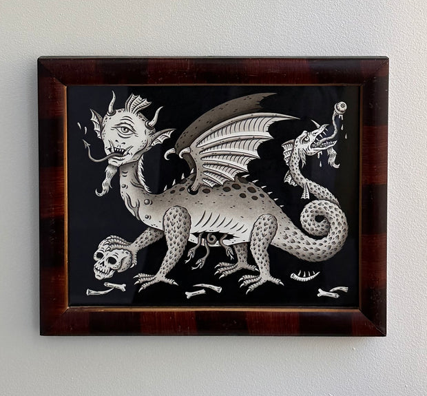 Greyscale illustration on black background of a dragon with a humanoid cyclops head and pointed tongue. It has snakes coming out of its stomach and a more traditional dragon's head coming out of its tail. It stands atop of a skull. Framed in wooden frame.