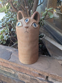Cat-shaped ceramic totem on a stone ledge with plants in the background