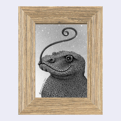 Finely rendered graphite drawing of a komodo dragon, seen only from the chest up. It smiles and has a curled tongue coming out its mouth. Piece is framed in a wood grain frame.