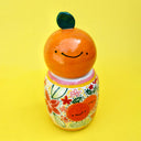 Ceramic sculpture comprised of 2 separate parts. Top is a rounded orange with a leaf and smiling cartoon face. Base is a rounded vase with many colorful paintings of fruits and flowers.