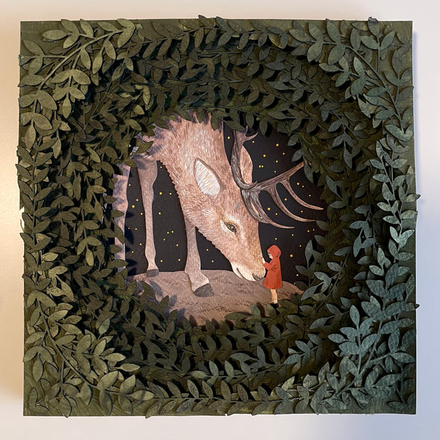 Layered cut paper diorama style sculpture, with many layers of leaves revealing a small scene of a red cloaked child petting the face of a very large Elk, which bows its head to the child.