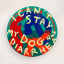 A round panel with a colorful dog illustration and the text 'I CAN'T STAY MY DOG HAS DIARRHEA' in raised cream lettering, mounted on a plain off-white wall.