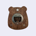 A capybara-shaped bottle opener made of medium brown wood grain with a circular brushed metal center and three round metal magnets, shown on a light gray background.