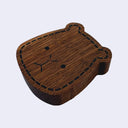 A small wooden capybara-shaped bottle opener with a dark brown wood grain finish, black stitched outline detail, and simple engraved facial features, shown on a plain light background.