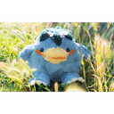 Blue plush doll of a rotund and chubby kappa, a creature with a large smiling yellow beak nose and leaves around a circle atop its head. The plush sits in a grassy field.