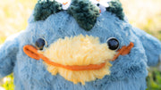 Blue plush doll of a rotund and chubby kappa, a creature with a large smiling yellow beak nose and leaves around a circle atop its head. 