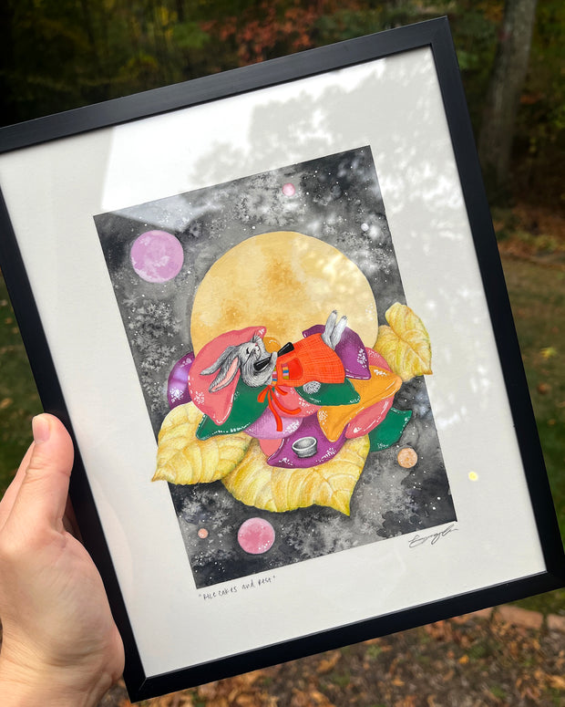 Illustration of a gray cartoon rabbit, wearing a red apron around the waist and laying atop a pile of cushions and yellow leaves. A large yellow moon and a dark sky is behind it.