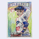 A hand-drawn colored pencil style illustration of a Los Angeles Dodgers baseball player wearing a white uniform with blue and red accents, with the word 'DODGERS' at the top and 'MIGUEL ROJAS' at the bottom, shown on a light gray background.