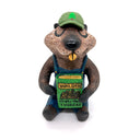 Sculpture of a beaver, dressed like a person in overalls and a green hat. It sits and holds Henry David Thoreau's "Walden"