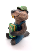 Sculpture of a beaver, dressed like a person in overalls and a green hat. It sits and holds Henry David Thoreau's "Walden"