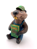 Sculpture of a beaver, dressed like a person in overalls and a green hat. It sits and holds Henry David Thoreau's "Walden"