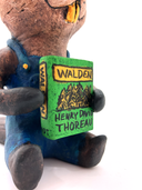 Sculpture of a beaver, dressed like a person in overalls and a green hat. It sits and holds Henry David Thoreau's "Walden"