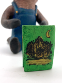 Sculpture of a beaver, dressed like a person in overalls and a green hat. It sits and holds Henry David Thoreau's "Walden"