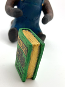 Sculpture of a beaver, dressed like a person in overalls and a green hat. It sits and holds Henry David Thoreau's "Walden"