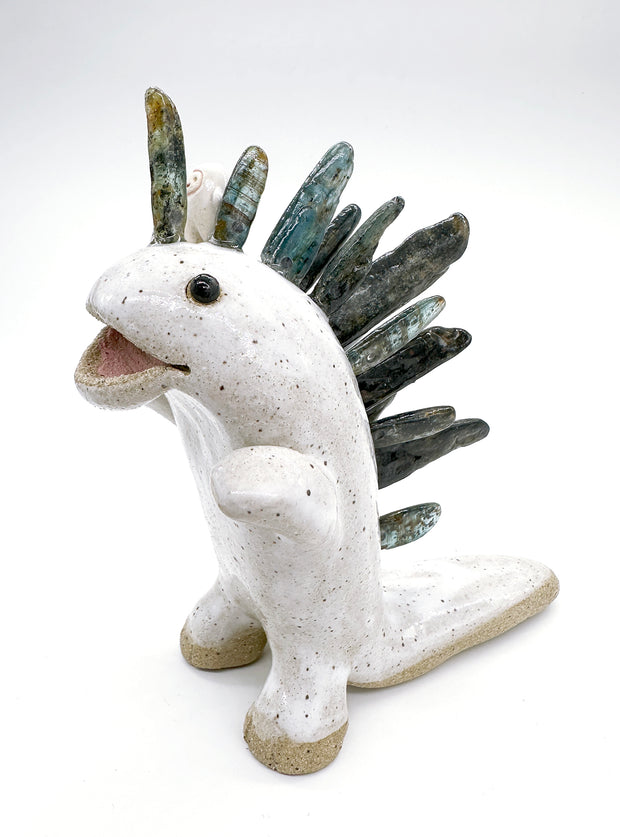 Ceramic sculpture of a white dinosaur with large spikes on its back made out of green and blue stones. A small, cute character stands atop its head and cheers.