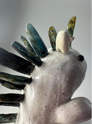 Ceramic sculpture of a white dinosaur with large spikes on its back made out of green and blue stones. A small, cute character stands atop its head and cheers.