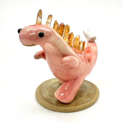 Ceramic sculpture of a pink dinosaur, mid stride, with orange quartz for spikes with a small character clinging to its tail. 