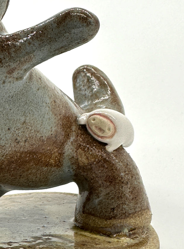 Ceramic sculpture of a brown and grey colored dinosaur with large quartz on its back like spikes. A small cute character clings on to the leg of the dinosaur.