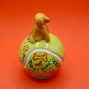 Ceramic sculpture of a small brown dog smiling and sitting atop a large tennis ball, with affirmations written on it with cute dog themed doodles.
