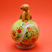 Ceramic sculpture of a small brown dog smiling and sitting atop a large tennis ball, with affirmations written on it with cute dog themed doodles.