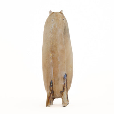 Ceramic sculpture of a tall brown character with tiny ears and eyes and stubby legs, no arms.