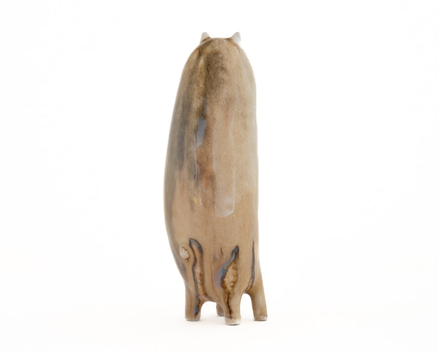 Ceramic sculpture of a tall brown character with tiny ears and eyes and stubby legs, no arms.