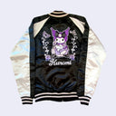 Shiny polyester bomber jacket with black body and white sleeves. Back has a large embroidered graphic of Kuromi sitting on a purple rose with more roses and butterflies next to her.
