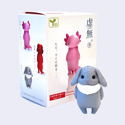 Small plastic figurine of a fluffy gray bunny standing straight up and looking off with a zoned out expression. Stands in front of its blind box.
