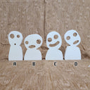 Wooden die cut sculpture of white ghost spirits with circular eyes and open smiles or mouth expressions. They stand side by side, 4 in total.