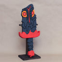 Sculpture of a stylized paddle or sword, modeled to look like Hedorah in dark gray, orange and red colorings.