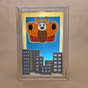 Shadowbox style artwork of a moth kaiju, floating over a cityscape with a blue background and light shining through.