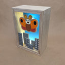 Shadowbox style artwork of a moth kaiju, floating over a cityscape with a blue background and light shining through.