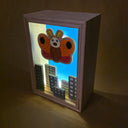 Shadowbox style artwork of a moth kaiju, floating over a cityscape with a blue background and light shining through.