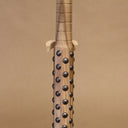 Wooden bat with black metal bumps evenly atop the surface, on a beige background. Close up to show detail in handle.