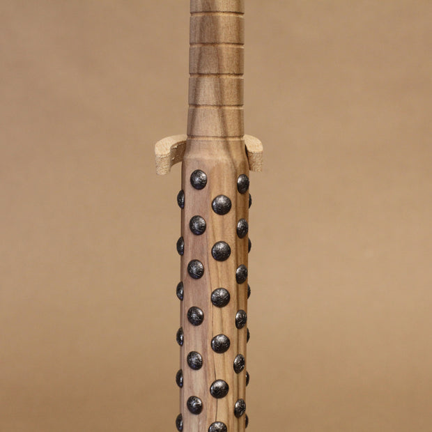 Wooden bat with black metal bumps evenly atop the surface, on a beige background. Close up to show detail in handle.