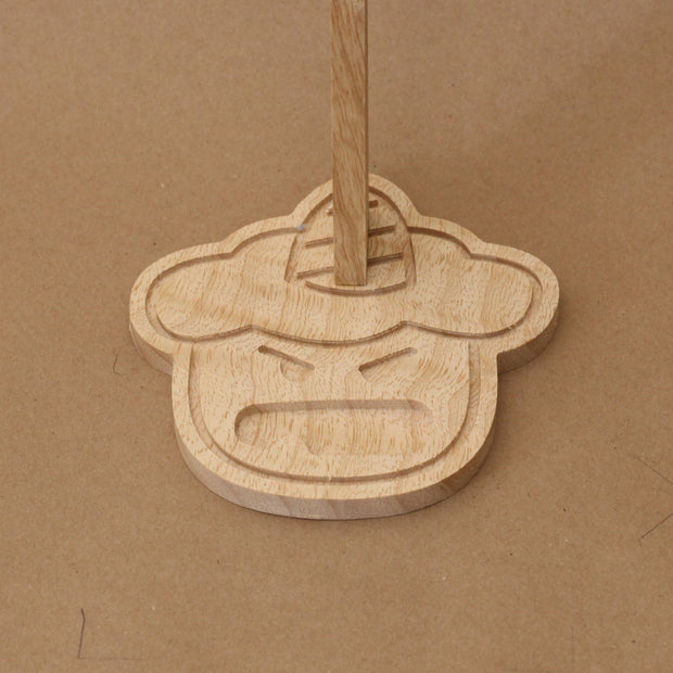 Close up of a wooden base shaped like a cartoon demon head, with a cute open mouth expression