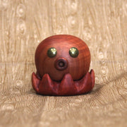 Wooden sculpture of a small octopus, with shiny metal eyes and an "o" shaped mouth. Its tentacles curl up towards itself.