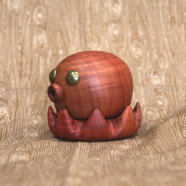 Wooden sculpture of a small octopus, with shiny metal eyes and an "o" shaped mouth. Its tentacles curl up towards itself.