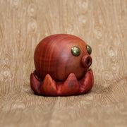 Wooden sculpture of a small octopus, with shiny metal eyes and an "o" shaped mouth. Its tentacles curl up towards itself.