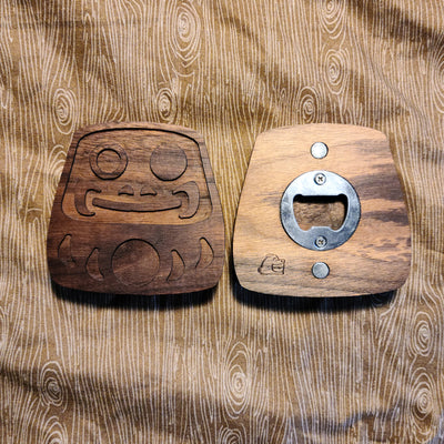 2 wooden bottle openers, one facing forward and the other backside up. Bottle opener is designed like a daruma and the backside displays the bottle opener and 2 magnets.