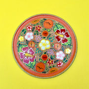 Ceramic plate with colorful surface paintings of fruits and tropical flowers. An orange ring frames the painted section of the plate.