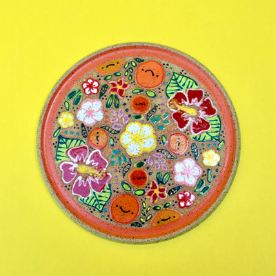 Ceramic plate with colorful surface paintings of fruits and tropical flowers. An orange ring frames the painted section of the plate.