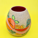 Ceramic sculpture on brown specked clay with a bright painting of an orange with a pink stripe running through it. Plants and other patterns are drawn as well.