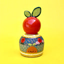 Ceramic sculpture of a bright colored orange, acting as a knob handle atop of an upside down dome shape. The dome has paintings of semi circle patterns and other oranges.