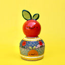 Ceramic sculpture of a bright colored orange, acting as a knob handle atop of an upside down dome shape. The dome has paintings of semi circle patterns and other oranges.