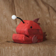 Whittled red wooden sculpture of an angler fish, with large cartoon type proportions. It has a light coming out of its head.