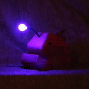 Whittled red wooden sculpture of an angler fish, with large cartoon type proportions. It has a light coming out of its head, emitting a purplish glow.